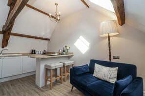 A loft-style room with a kitchen area, a blue sofa, and a chandelier. - The Old Dairy, Nettleton (Chippenham)