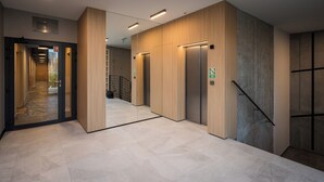Un interior moderno con un pasillo que lleva a ascensores, una escalera y una puerta de cristal.