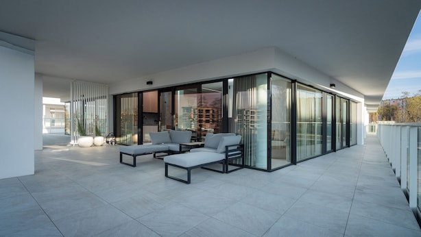 Un espacio exterior moderno con una zona cerrada por vidrio, un área de estar con sofás y vistas a la ciudad.