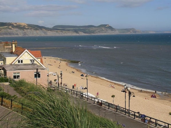 Une plage côtière avec une promenade, un bâtiment doté d’un toit rouge et une vue dégagée sur la mer.
