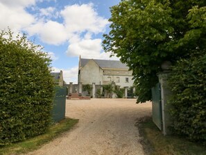 Une allée de gravier mène à un bâtiment doté d’une grande entrée et d’un porche abrité.
