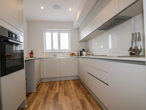 A modern kitchen with white cabinets, a stainless steel oven, and a window providing natural light. - The Sand Dunes, Crantock (Crantock)