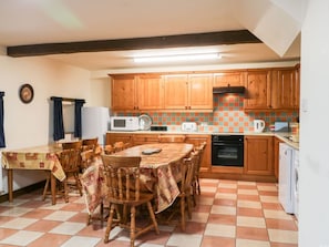 A kitchen with wooden cabinets, a tiled backsplash, a dining table with chairs, and a microwave. - Byre Cottage, Flyingthorpe (Whitby)