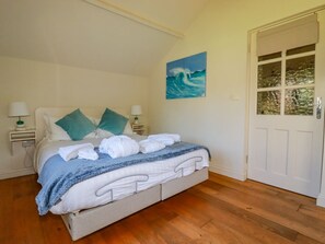 Ein Schlafzimmer mit Bett, Kissen, einem Gemälde, einem Nachttisch, einer Lampe und einer Tür.