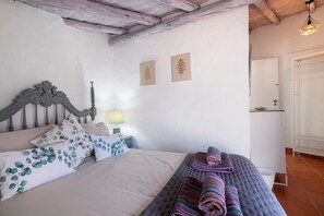 Un dormitorio con cama, almohadas, una mesita de noche con lámpara y una obra de arte en la pared.