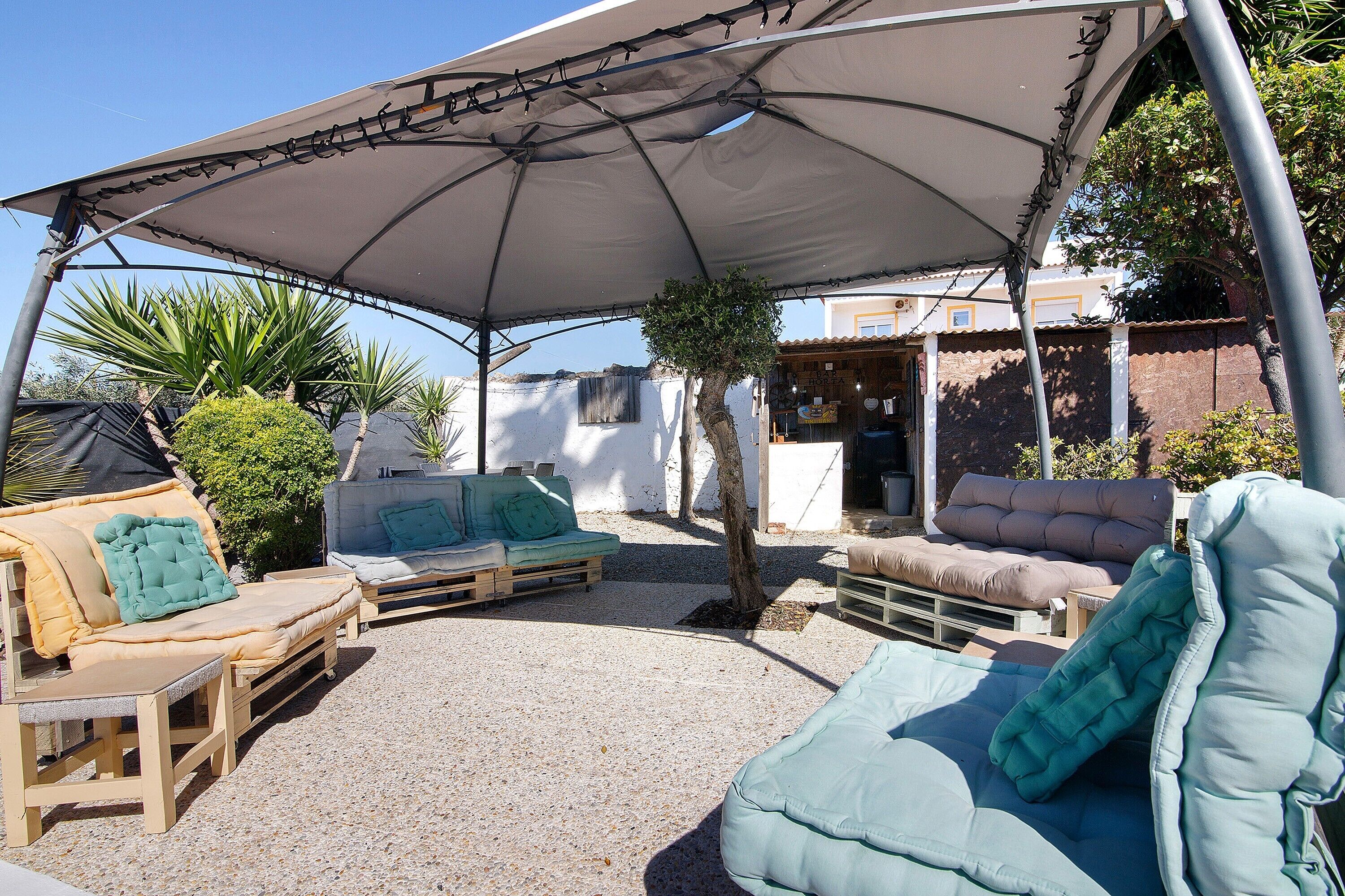 An outdoor seating area with a covered patio, wooden furniture, and a small tree.