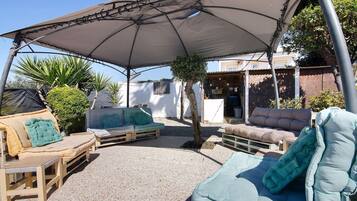 An outdoor seating area with a covered patio, wooden furniture, and a small tree.