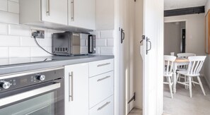 A modern kitchen with white cabinets, a microwave, an oven, and a dining area with white chairs and a table. - WASTWATER, woodburning stove, in Sawrey (Ambleside)