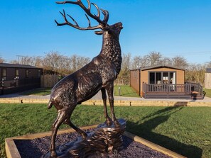 A bronze deer statue in a landscaped area with a wooden deck and a building in the background. - Meadows Park 2, Hornsea (Hull)