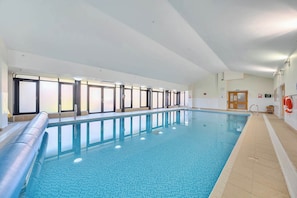 Une piscine intérieure avec un sol carrelé, un escalier métallique et une porte en bois dotée de panneaux de verre.