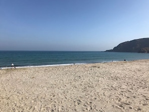 A beach with a clear sky, sandy shore, and a distant cliff.