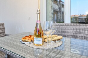 A glass table with a bottle of wine, a glass, and pastries on a woven placemat. - MGH- Gardenia Holiday Home (Castelnuovo del Garda)