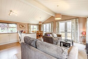 A spacious living area with a sofa, a dining table with chairs, a kitchen area with a washing machine, and large windows with curtains.