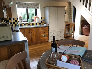 A kitchen with wooden cabinets, a white refrigerator, a dining table with chairs, a wicker basket with bread, and a bottle of wine. - Oak Cottage, Newcastle Emlyn (Llandysul)