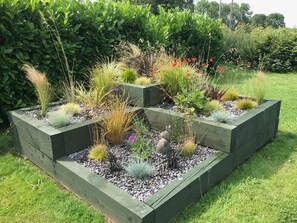 A garden with raised wooden planters containing various plants and a decorative squirrel statue. - Oak Cottage, Newcastle Emlyn (Llandysul)