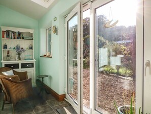 A room with a white bookshelf, wicker chair, and a glass door leading to a garden. - Rose cottage, Cromer (Cromer)