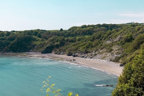 Kystlandskab med strand, klippepartier og frodig vegetation.