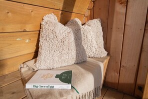 A wooden bench with a beige blanket and a book titled 'Big Green Egg' by James Whittlore. - Glamping Pod 4 Truce Yorkshire (Scarborough)