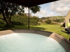 Ein Whirlpool unter einer Pergola mit Blick auf eine Wiese und Hügel im Hintergrund.