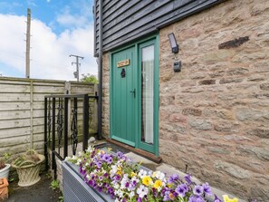 A stone building with a green door, a flower bed with various flowers, and a wooden fence.