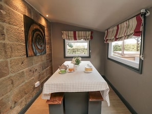 A room with a stone wall, a checkered tablecloth, a window with curtains, and a stone wall art piece. - Swang Cottage, Glaisdale (Whitby)