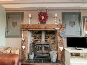 A rustic fireplace with a stone wall, a wooden mantel, and a television on a white stand. - Swang Cottage, Glaisdale (Whitby)