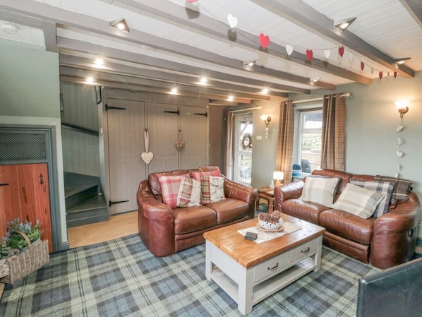 A cozy living room with a brown leather sofa, plaid rug, and a wooden coffee table. - Swang Cottage, Glaisdale (Whitby)