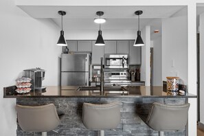A modern kitchen with a central island, stainless steel appliances, and pendant lighting. - Clubhouse Suite | Golf & Water View | 85” TV (Branson)
