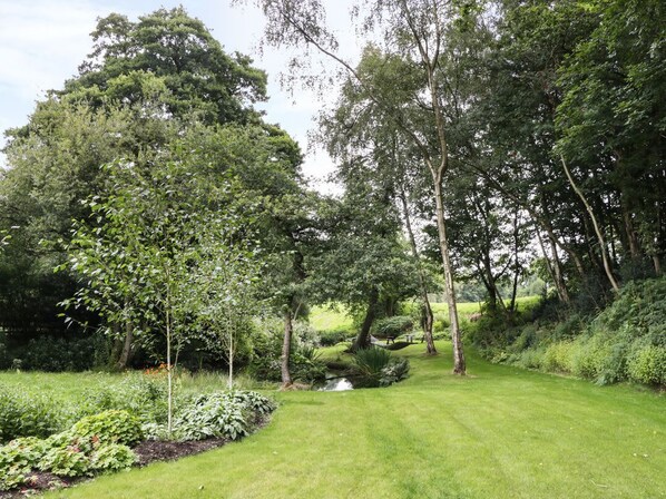 A lush garden with a variety of trees and shrubs, a small stream, and a well-maintained lawn.