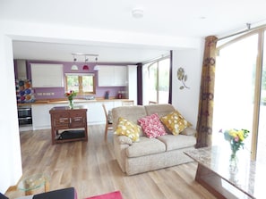 A modern living room with a sofa, a glass coffee table, and a view of the kitchen.