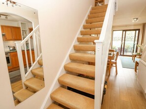 A staircase with carpeted steps leading to a kitchen area with wooden cabinets and a dining table. - Poole Quay Cottage, Poole (Poole)