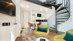 Een modern appartement met een spiltrap, een keuken en een woonruimte met gele stoelen en een salontafel.