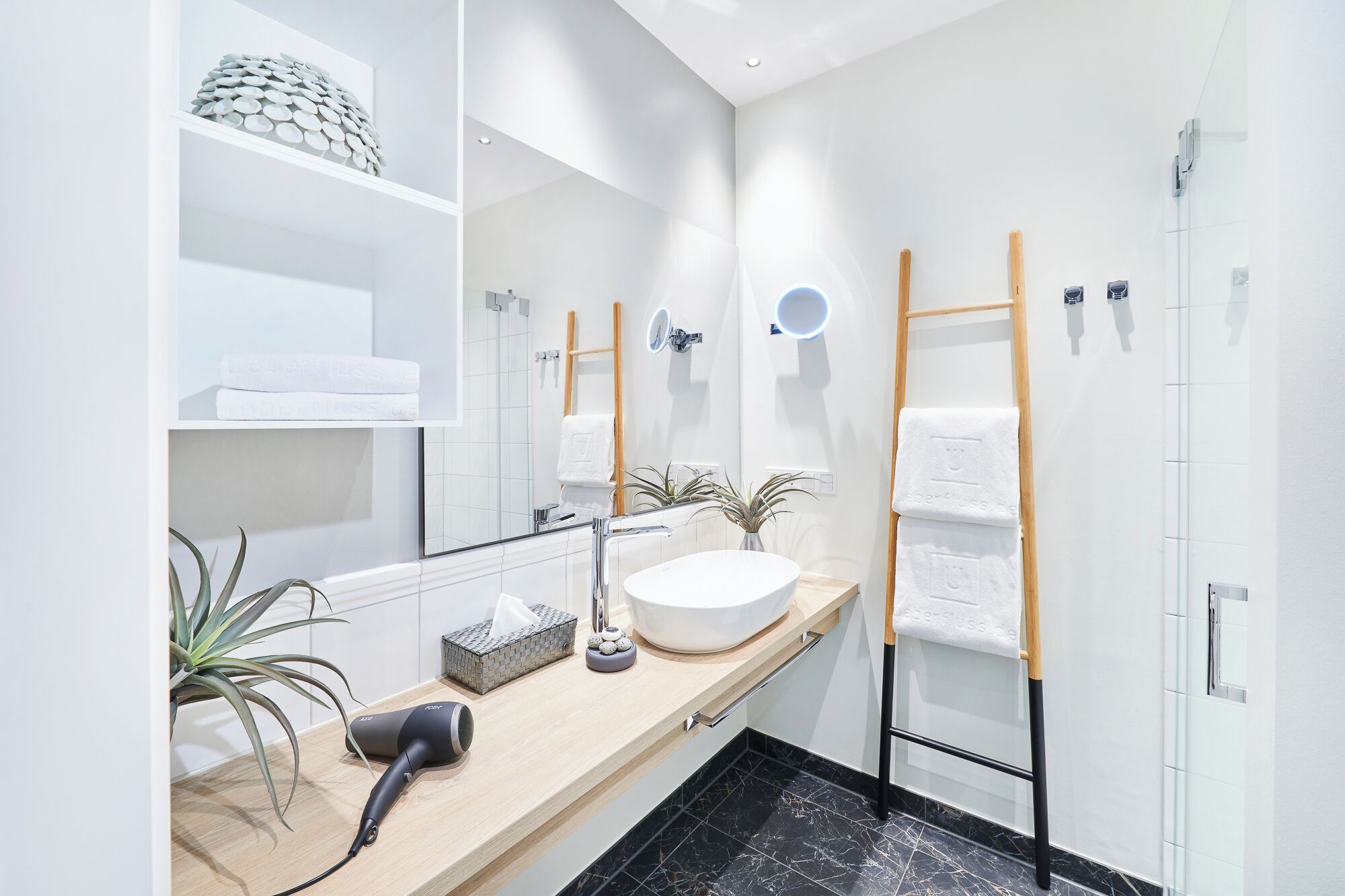 Uma casa de banho moderna com um espelho grande, uma pia redonda, um porta-toalhas, um secador de cabelo e uma planta em vaso.
