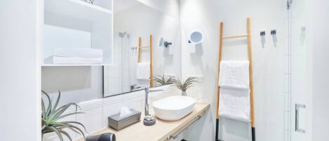 Uma casa de banho moderna com um espelho grande, uma pia redonda, um porta-toalhas, um secador de cabelo e uma planta em vaso.