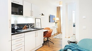 Een moderne keuken met witte kasten, een zwart aanrecht en een spoelbak. Er is een eethoek met een tafel en stoelen, en een zithoek met een bank en plaid.