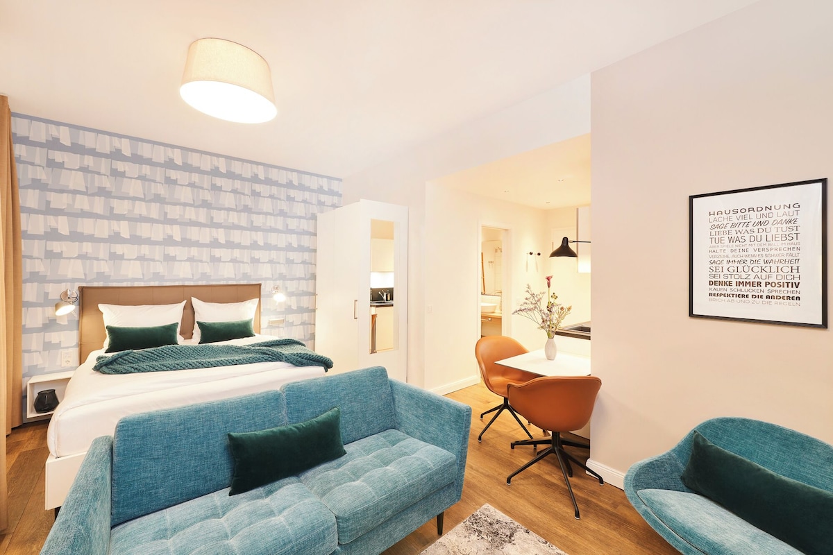 Een moderne hotelkamer met een bed, een blauwe bank, een bureau en een citaat in een lijst op de muur.