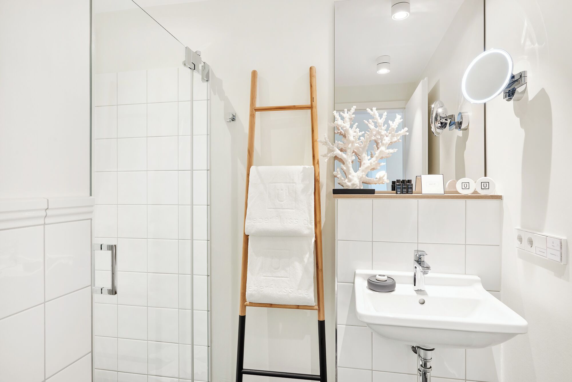 A modern bathroom with a shower, a wooden ladder, a sink, and a mirror with lights.