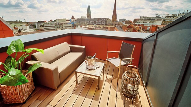 Een terras op het dak met een beige bank, een stoel, een kleine tafel en een potplant.