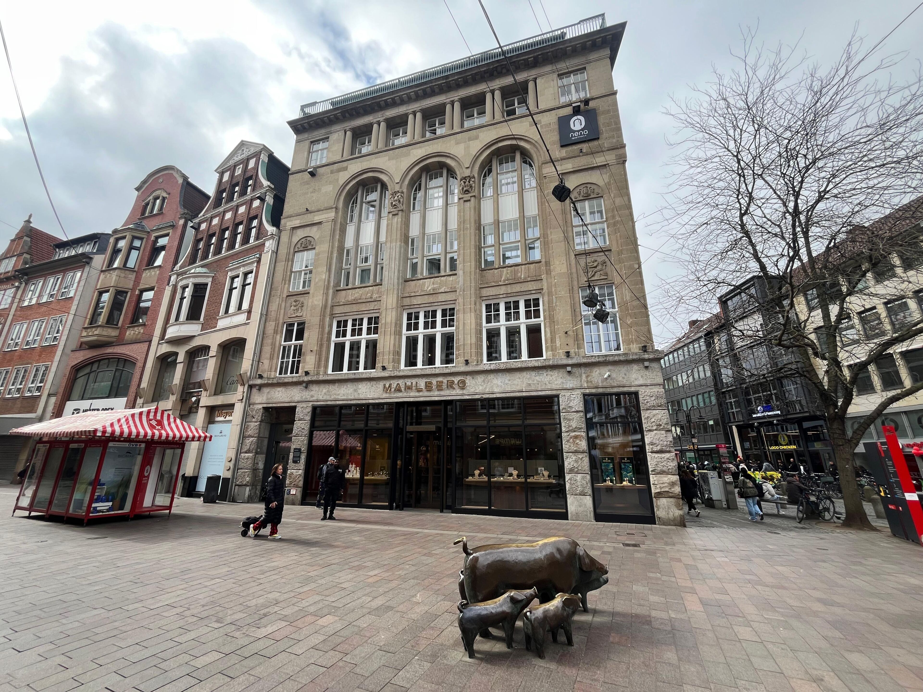 Un edificio histórico con un llamativo letrero 'MAHLBERG', ventanas grandes y una estatua de una vaca y un cerdo en primer plano.