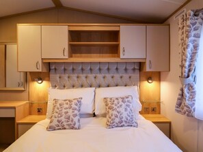 Une chambre à coucher avec un grand lit, deux tables de chevet, une tête de lit avec espace de rangement et une fenêtre avec un rideau.