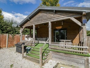 Eine Holzhütte mit überdachter Veranda, Grill und kleiner Terrasse.