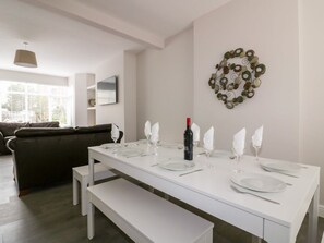 Un coin repas avec une table blanche dressée pour quatre personnes, une bouteille de vin et un élément décoratif mural.