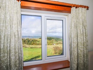 Ein Fenster mit zwei Scheiben, Vorhängen und einem Holzbalken darüber.