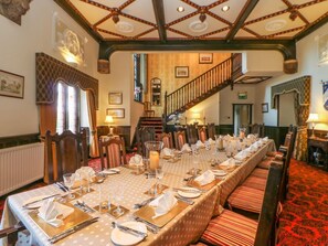 Une longue table à manger, dressée pour un repas, avec des chaises de chaque côté, dans une pièce dotée d’un escalier et d’un tapis à motifs.
