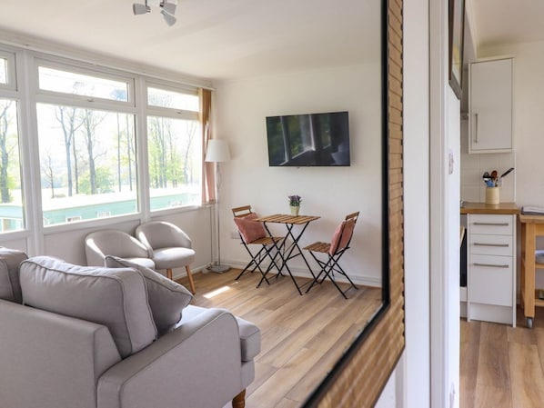 Una sala moderna con un sofá, una mesa de comedor con sillas, un televisor en la pared y una zona de cocina con armarios y una encimera.