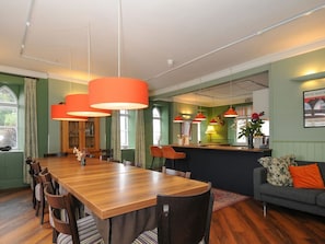 Un comedor con mesa y sillas de madera, una zona de bar con taburetes, y un sofá con un cojín naranja.