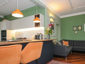Una cocina moderna con una isla central, luces colgantes, un sofá gris y suelo de madera.