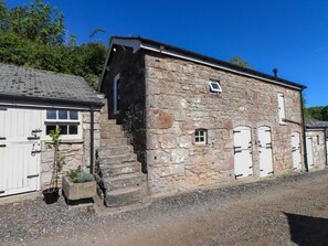 A stone building with a small window, a door, and a staircase leading to an upper level.