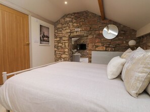 A bedroom with a stone wall, a bed with white bedding, a wooden door, and a mounted mirror.