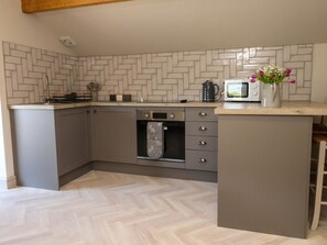 A compact kitchen with grey cabinets, a microwave, and a kettle on the countertop.